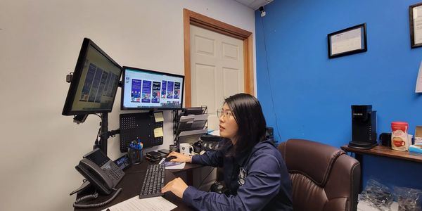 Woman working at a dual-monitor computer setup in an office.
