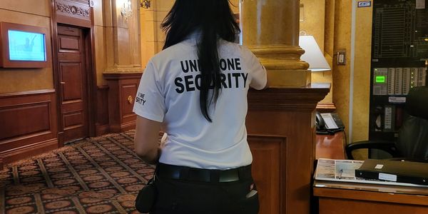 A female security guard standing in an ornate indoor hallway.
