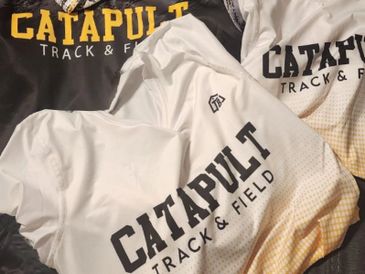 Three Catapult Track &amp; Field shirts in black, white, and cream colors.