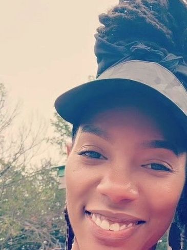 A smiling woman wearing a visor with her hair tied up outdoors.