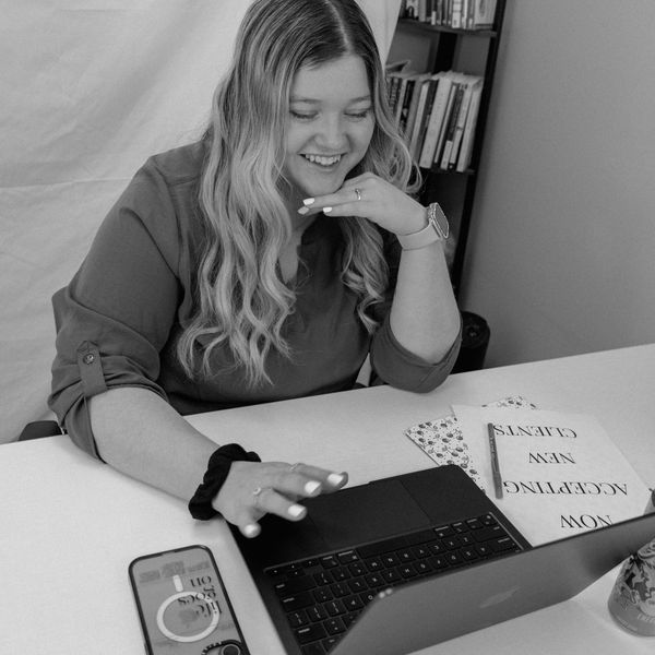 A smiling woman working on a laptop at a desk with phone and papers.