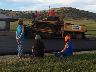 Children watching a man on a yellow road roller.