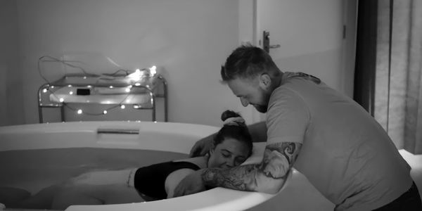 Relaxed and calm women in labour in a bath with her partner supporting her with the hypnobirthing te