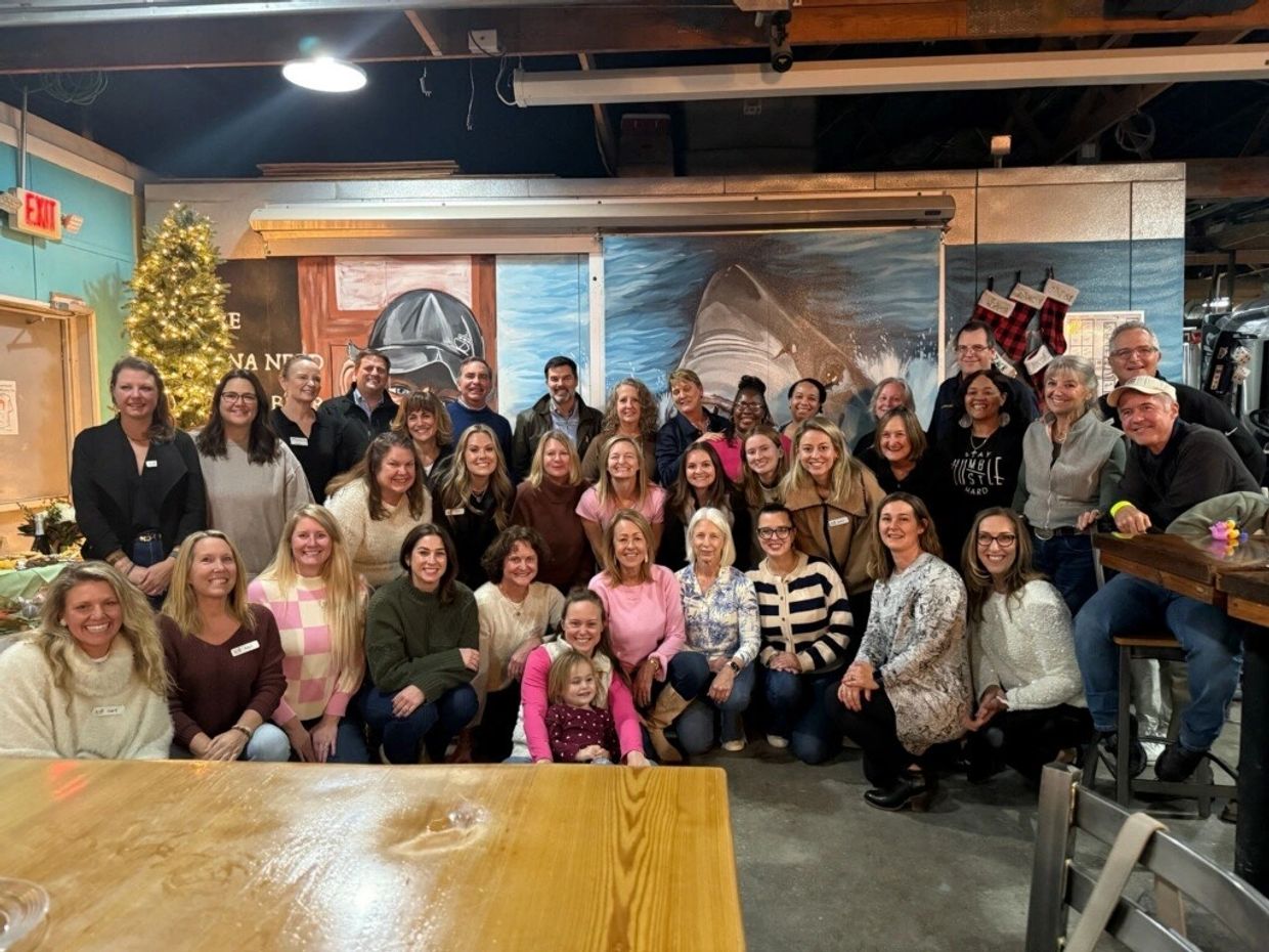 Large group of people posing indoors with holiday decorations and a mural in the background.