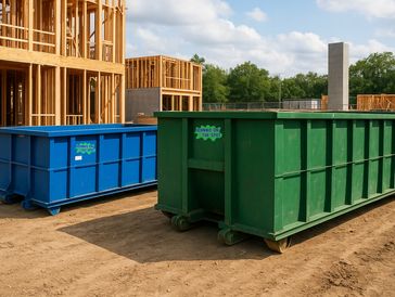 Large blue and green dumpsters on a construction site with wooden building frames.