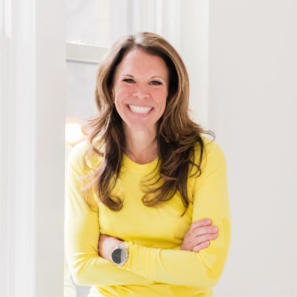 Woman in yellow shirt smiling with arms crossed.