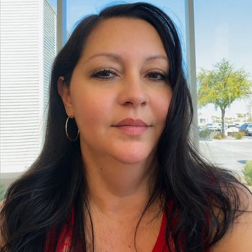 Woman with dark hair and hoop earrings indoors near a window.