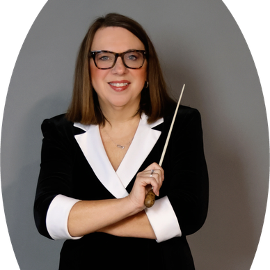 A woman in glasses holding a conductor's baton, smiling confidently.