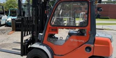 Orange Toyota forklift parked outdoors under a partly cloudy sky.