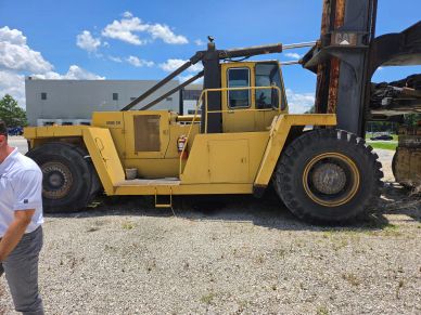 Large yellow industrial forklift on gravel with person nearby.
