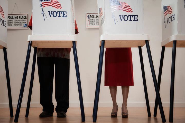 Two people voting privately in booths with American flags.