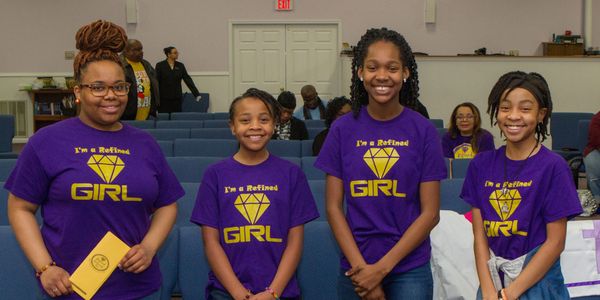 Four girls smiling in purple 'I'm a Refined Girl' shirts inside a church.