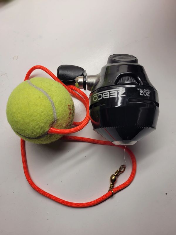 Fishing reel attached to a tennis ball with a red cord.