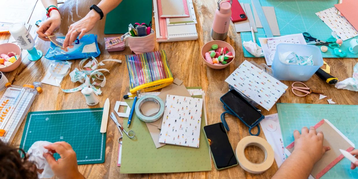 People crafting at a table with various tools and supplies.