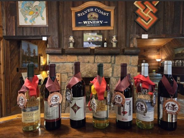 Seven decorated wine bottles displayed on a wooden counter at Silver Coast Winery.