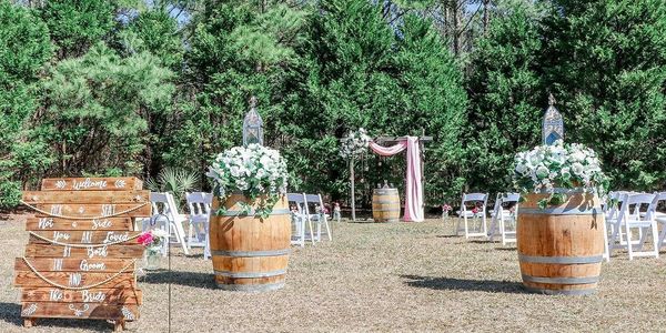 Rustic outdoor wedding setup with floral barrels and wooden sign.