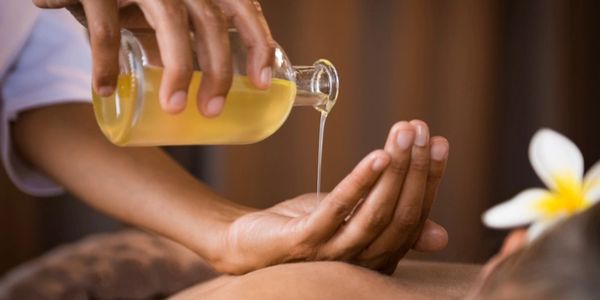 Hand pouring massage oil from a glass bottle onto another hand.