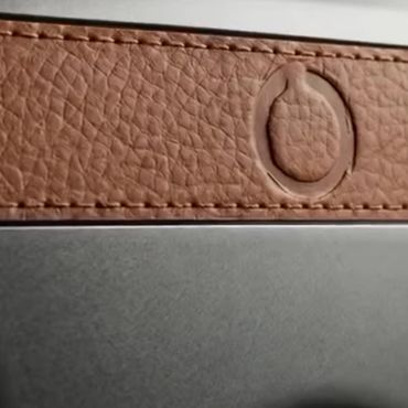 Close-up of a textured brown leather band with stitching and embossed circular logo.