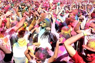Crowd celebrating Holi festival with vibrant colored powders.