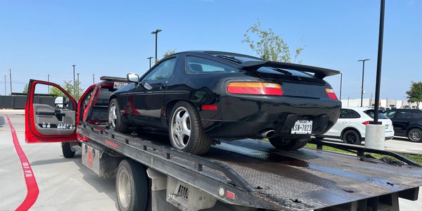 Black Porsche on a tow truck on a sunny day.