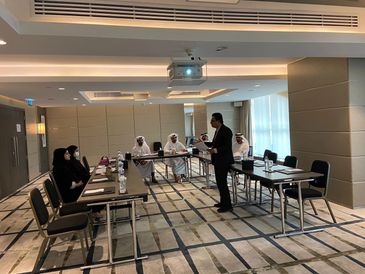 A meeting with a man presenting to seated attendees in traditional attire and business wear.