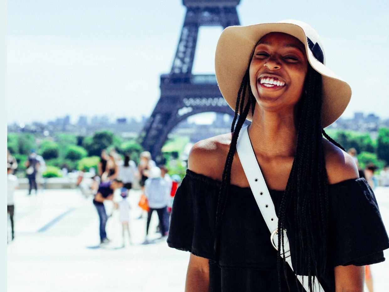 Smiling woman in hat near Eiffel Tower.
