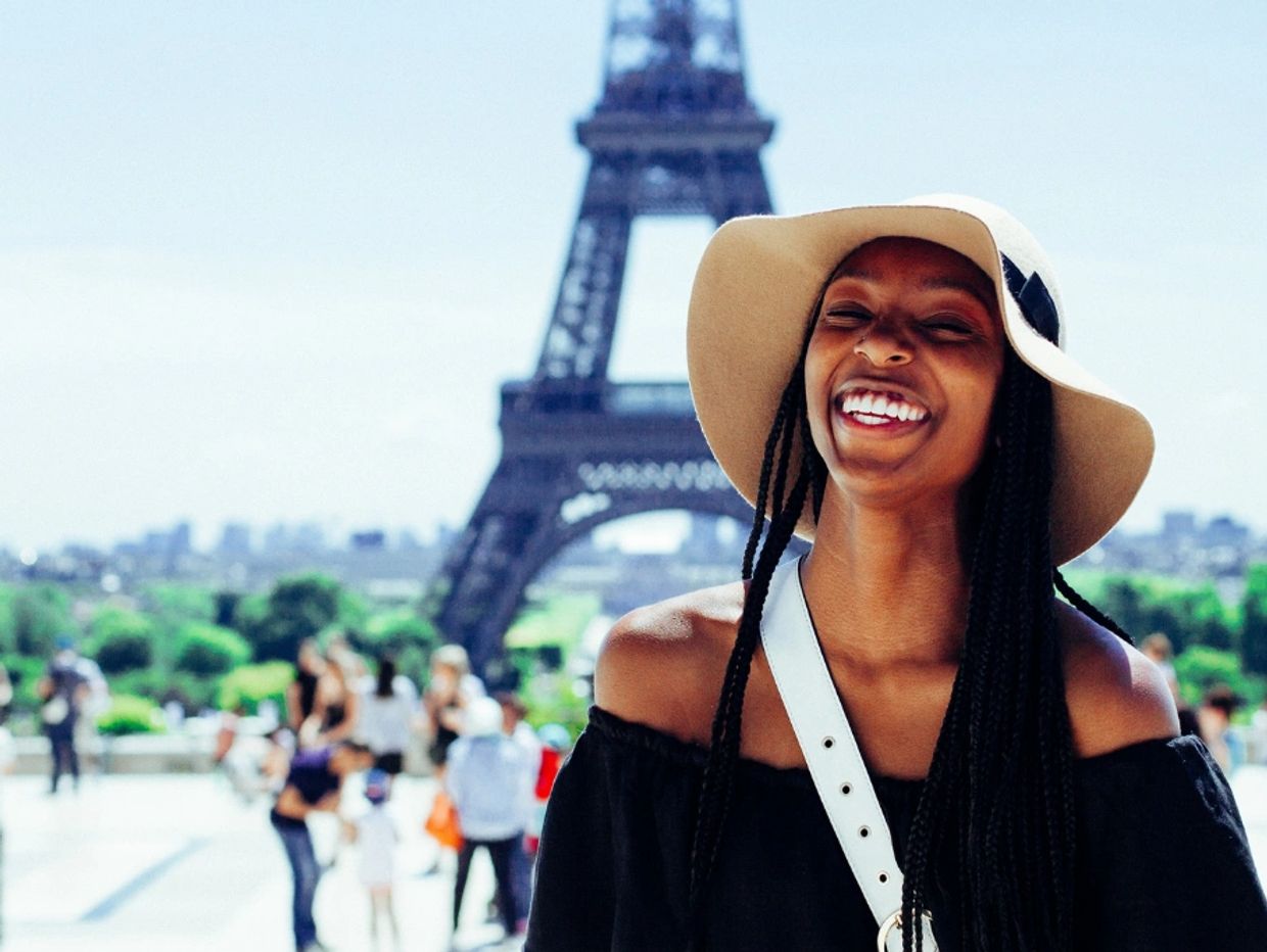 Smiling woman in a hat near the Eiffel Tower.