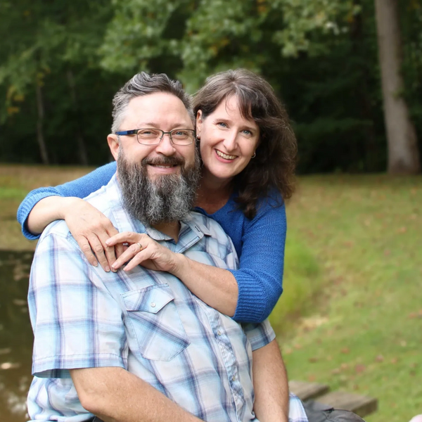 Marcy hugging Chris outside by a pond.