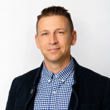Professional man in checkered shirt and dark jacket smiling.