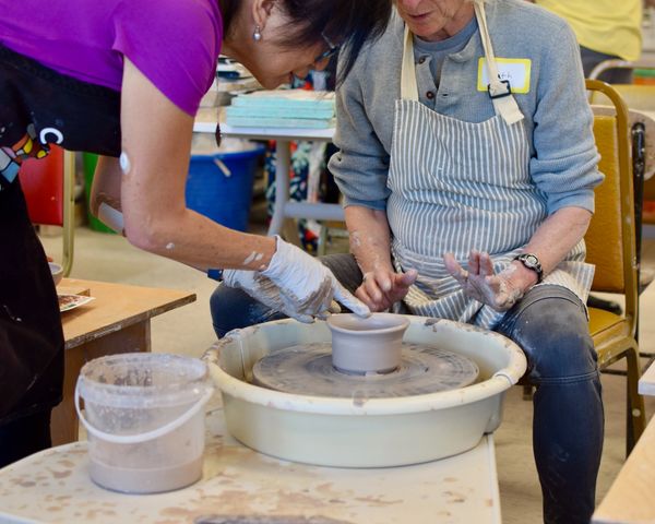 Two people shaping clay on a pottery wheel during a pottery class.