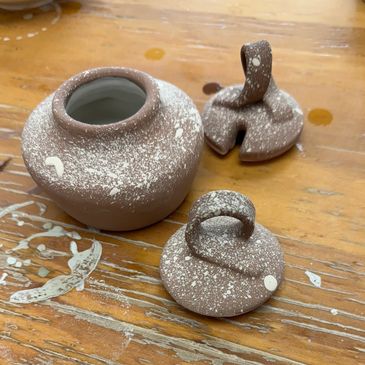 A ceramic jar with two lids placed next to it.