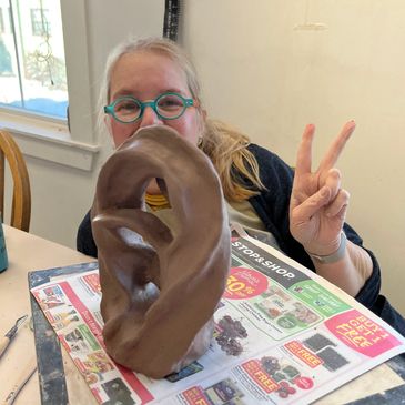 A student holds up a peace sign behind her sculpted piece