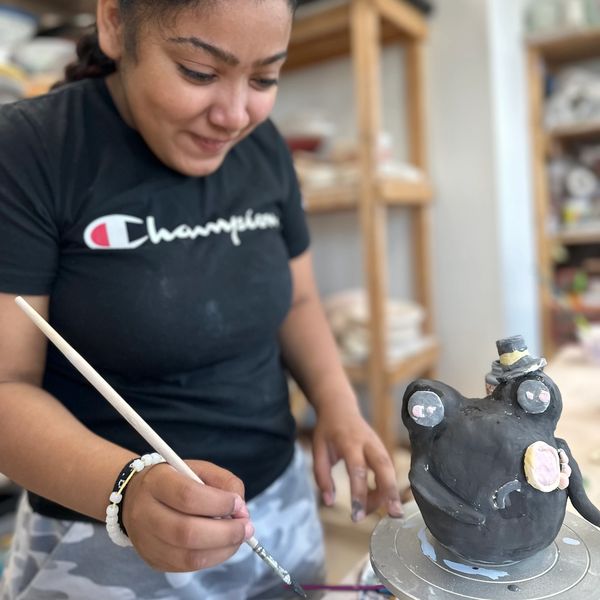 A student paints details on her artwork that resembles a frog wearing a top hat