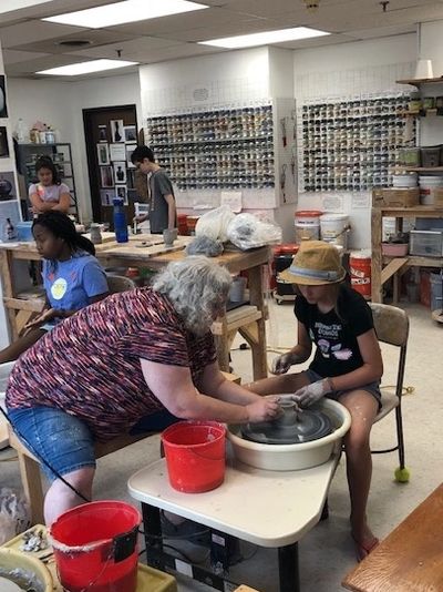 An instructor helps a child with their pottery