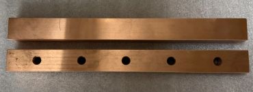 Two copper bars, one solid and one with five holes.