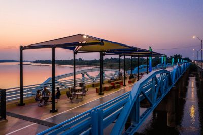 People sitting under a canopy on a bridge at sunset.
