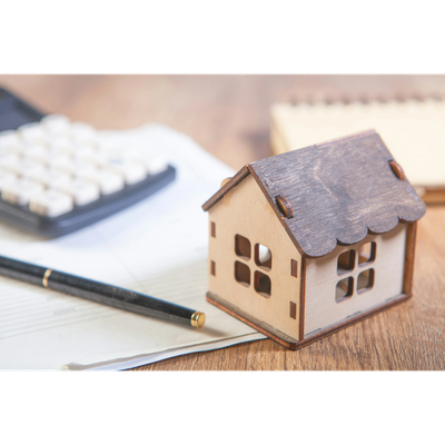 Small wooden house model with pen and calculator on paperwork.