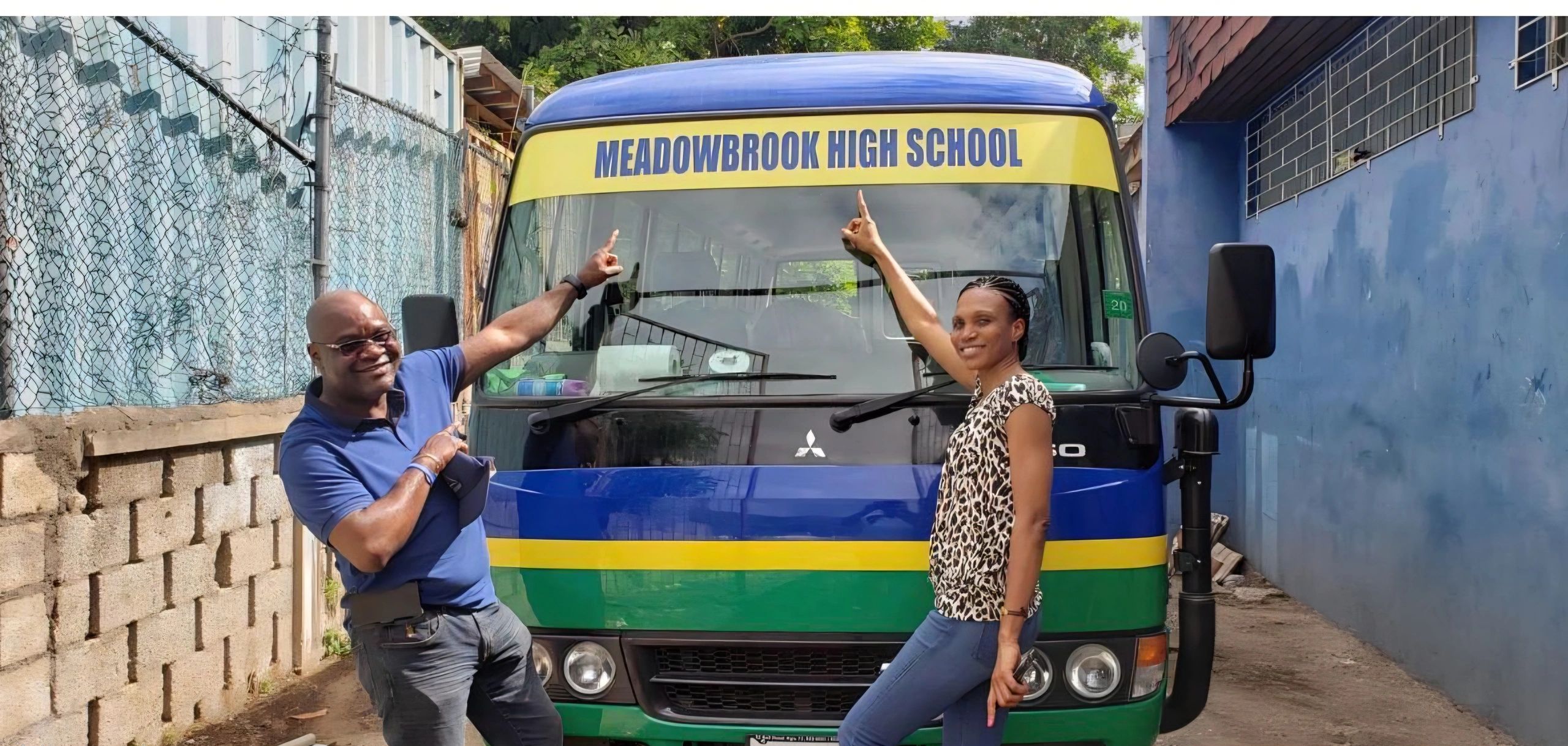 Two people pointing at a Meadowbrook High School bus.