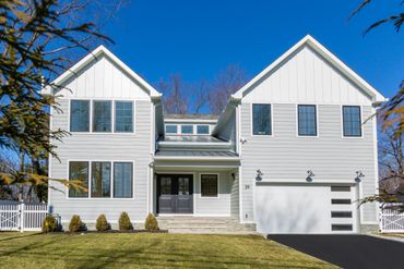 Modern white two-story house with a spacious front yard and clear blue sky.