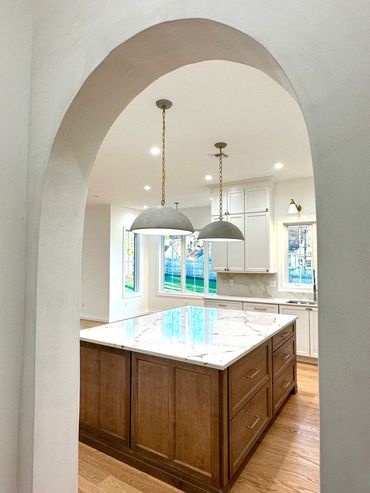 Modern kitchen with a large marble island and pendant lights under an archway.