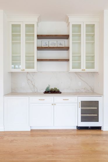 Minimalist white kitchen area with glass cabinets and wooden shelves.