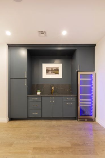 Modern kitchenette with dark gray cabinets and a wine cooler with blue lighting.