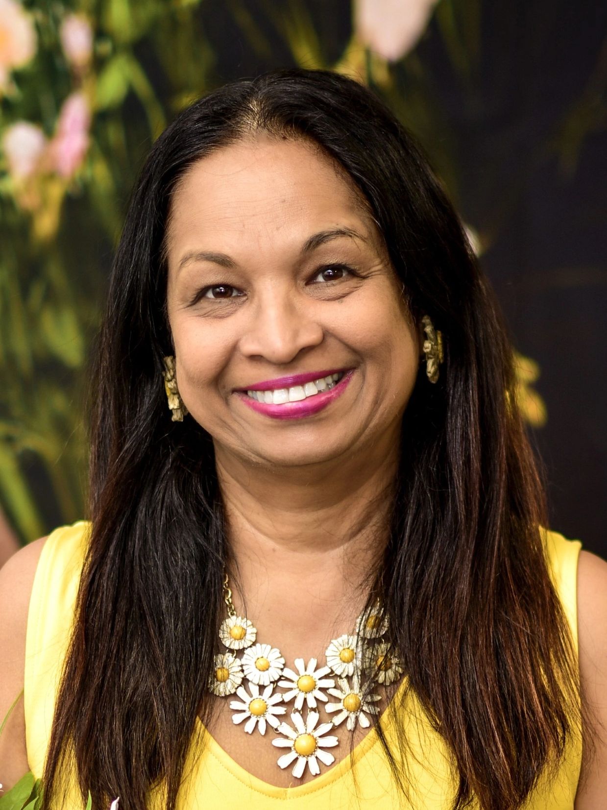 Smiling woman wearing a yellow top and daisy necklace.