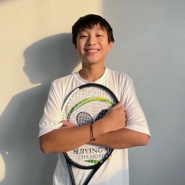 Boy smiling with tennis racket and white shirt.