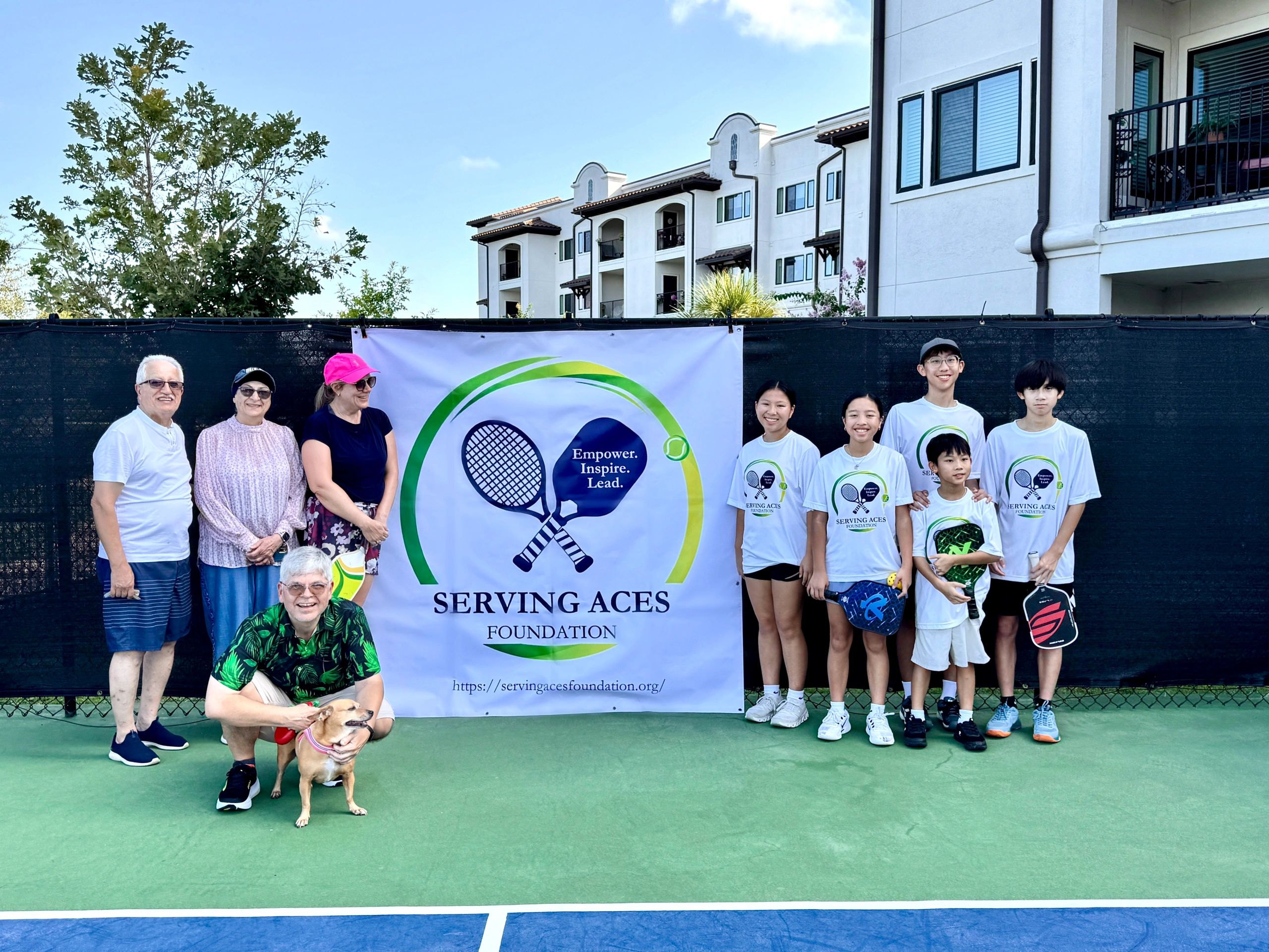 Group photo on a tennis court with Serving Aces Foundation banner.