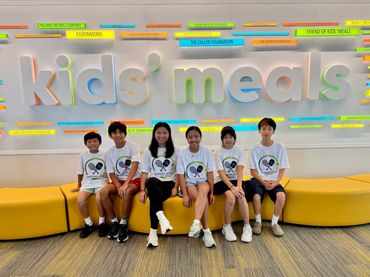Group of kids sitting in front of a colorful kids meals sign.