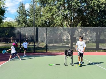 Kids playing tennis on an outdoor court.