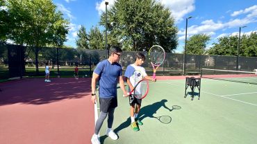 A tennis coach teaching a young player on court.