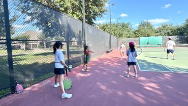 Kids waiting to play tennis on an outdoor court.