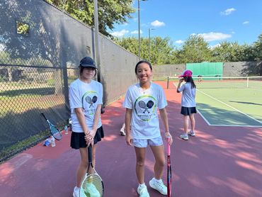 Three girls on a tennis court holding rackets.